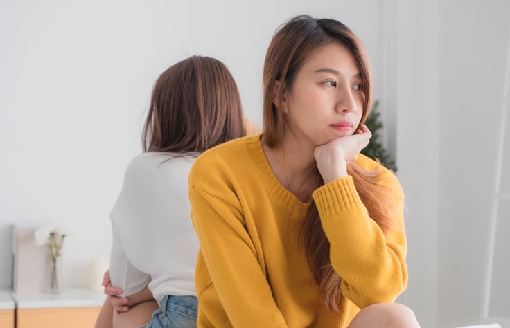 Two female friends sitting back to back.