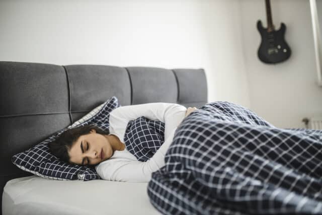 Young woman lying down on her bed in pain.