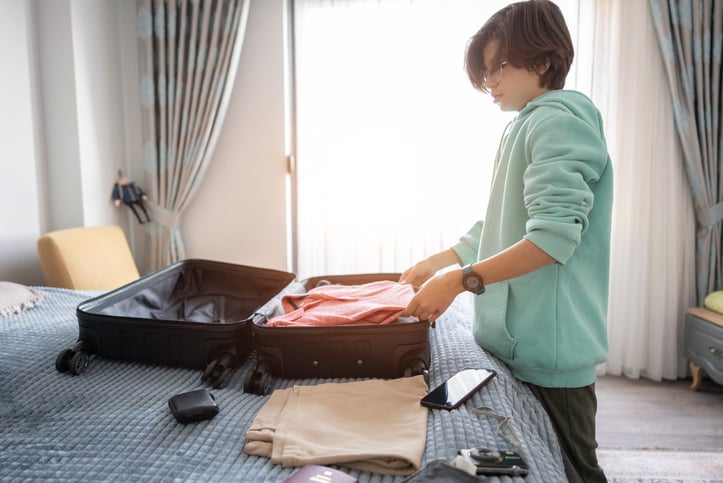 Young boy packing his suitcase on bed.