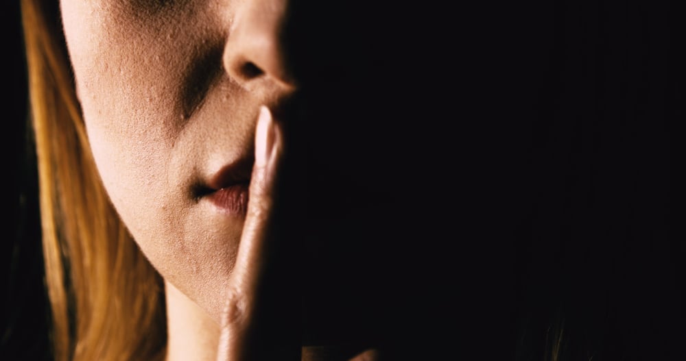 Woman places her finger over her mouth in silence.
