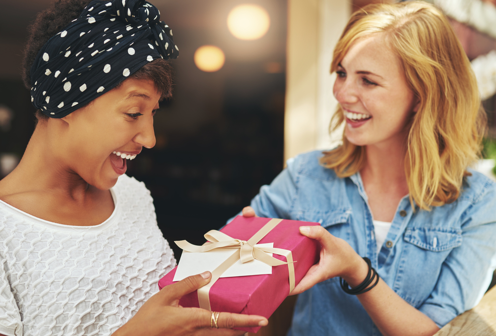 A blond woman giving a gift to her friend