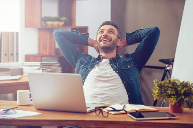 guy leaning back at desk with hands on heads