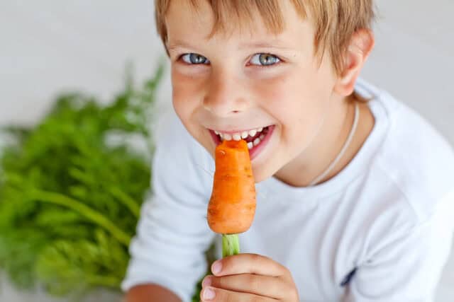 Little boy eating a carrot.