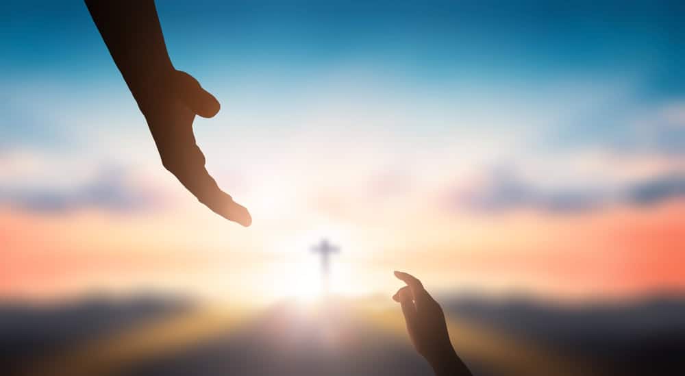 Two hands and a cross in the distance.