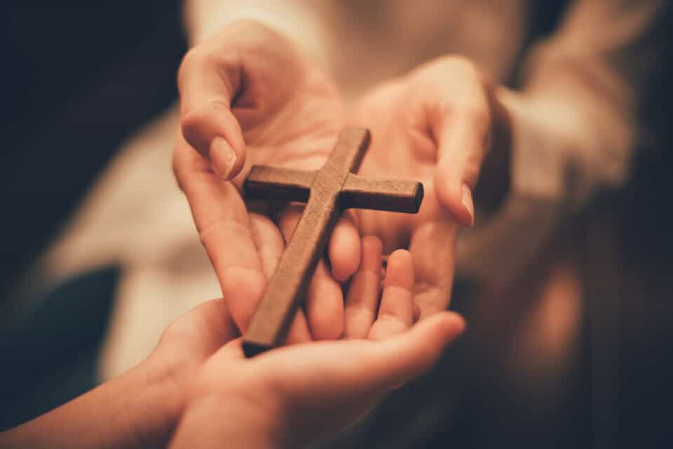 Hands holding a wooden cross.