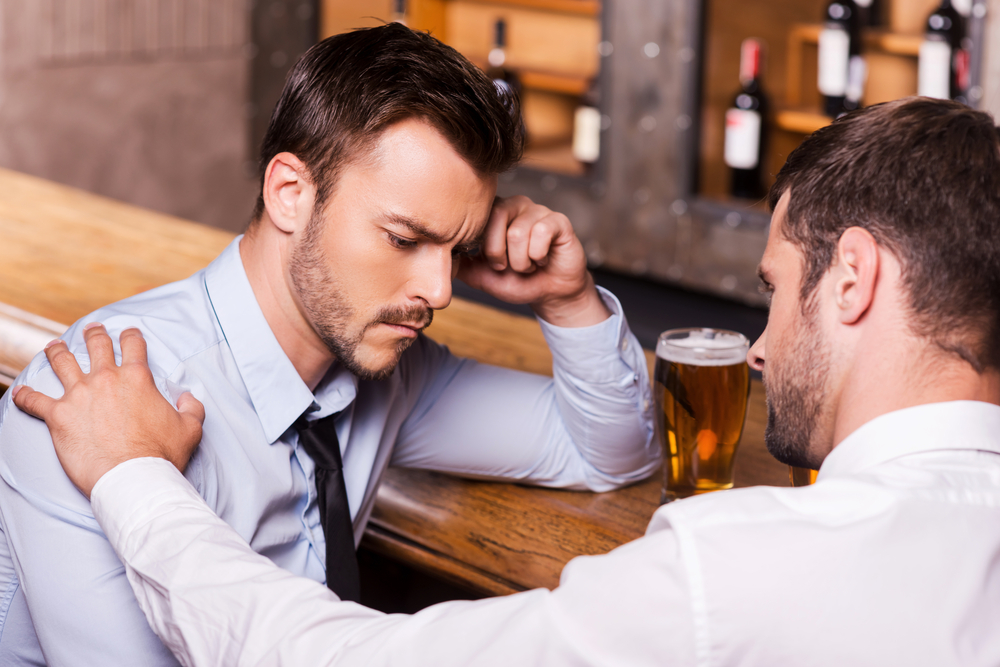 A young business man consoled by his male friend at the bar