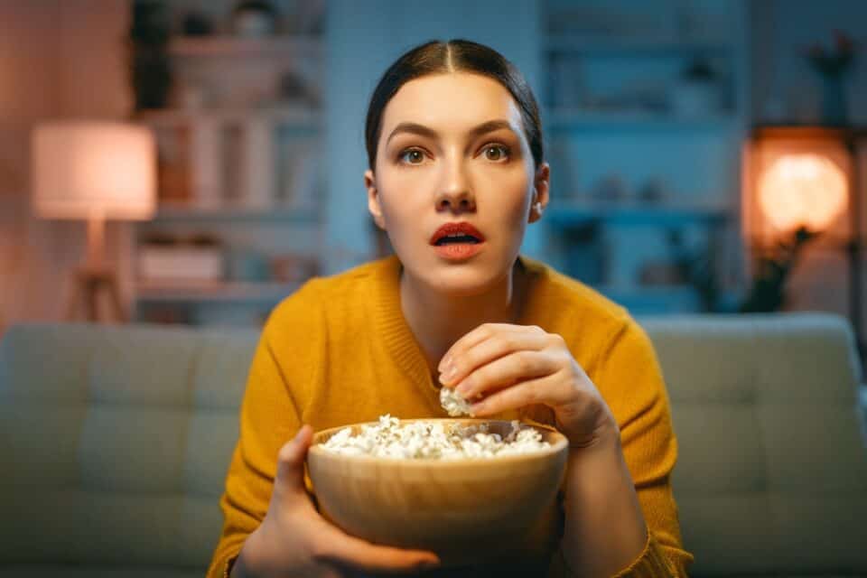 Woman watching TV eating popcorn.