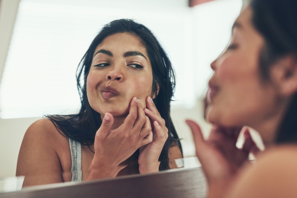 Woman looking at her pimple in the mirror.