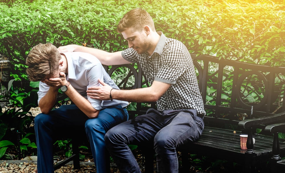 A young man is being consoled by his male friend