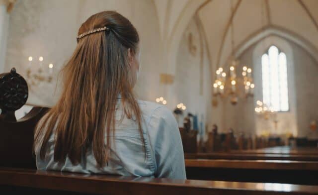 Woman sitting in a pew at church praying.