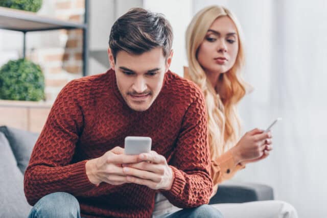 Woman looking over boyfriend's shoulder at his phone.