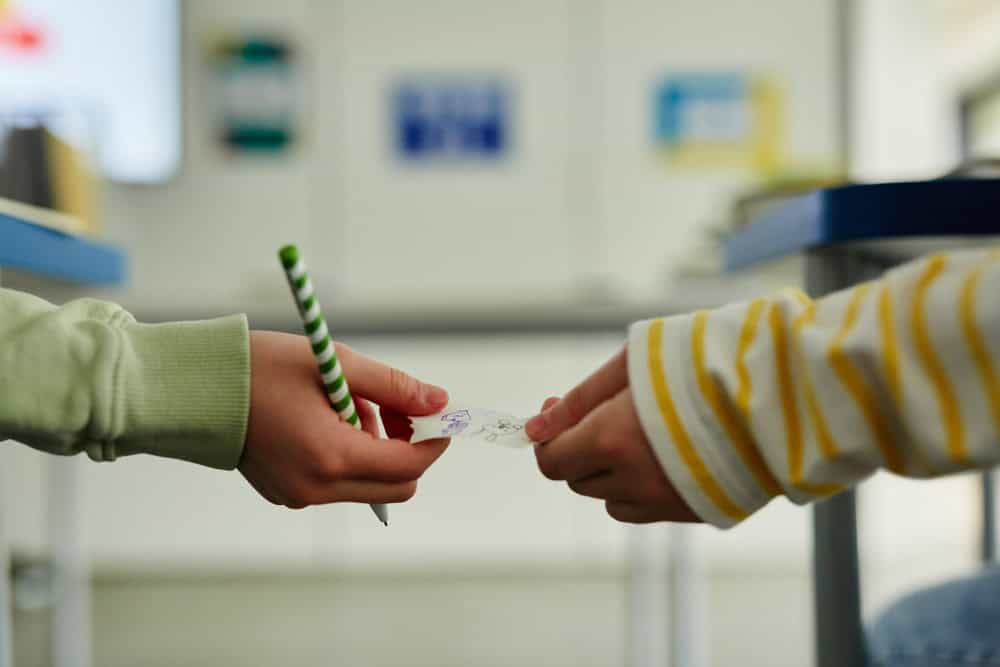 Two girls pass a Pot-it Note. 