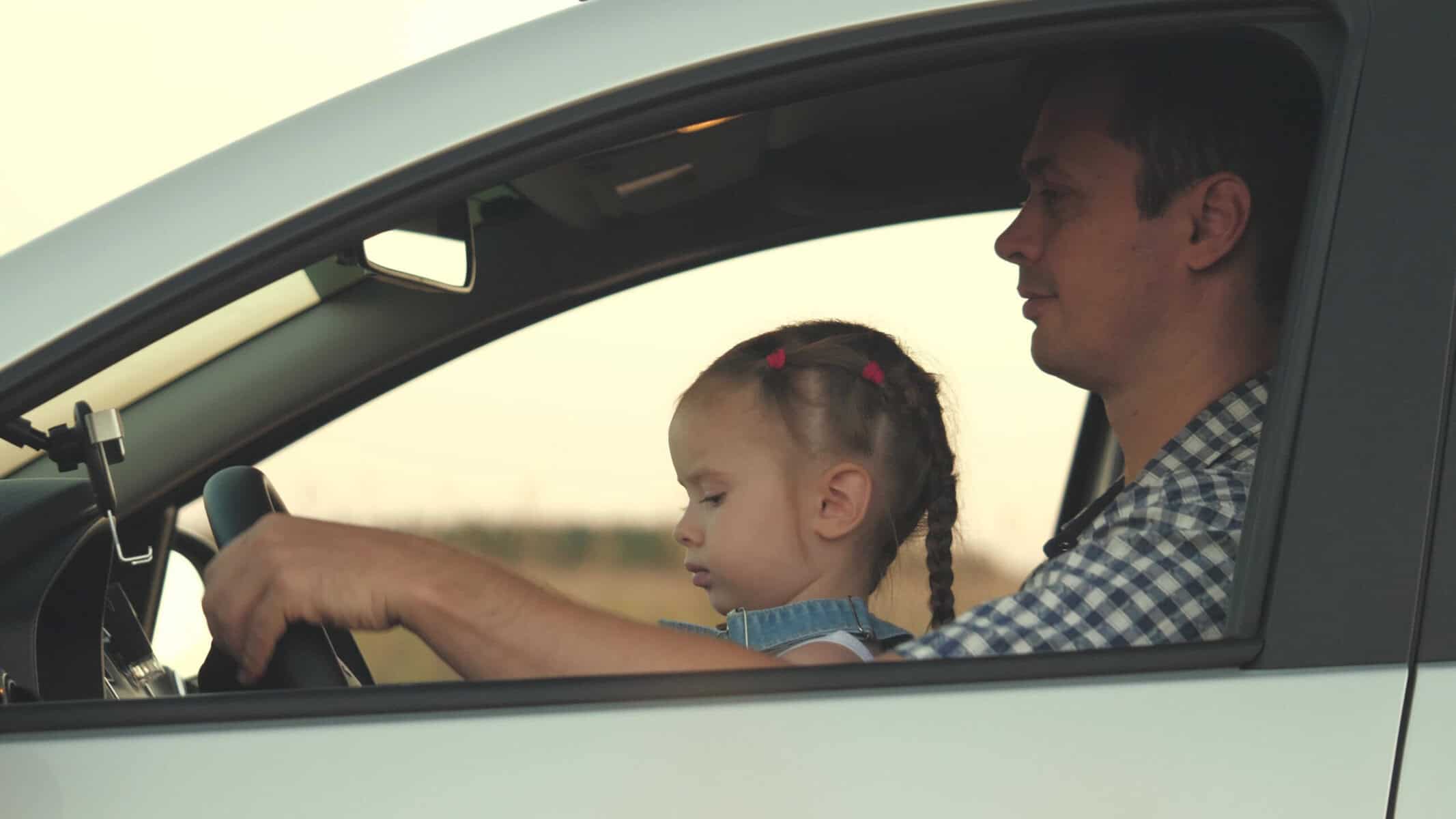 Dad with his daughter at the wheel of car.