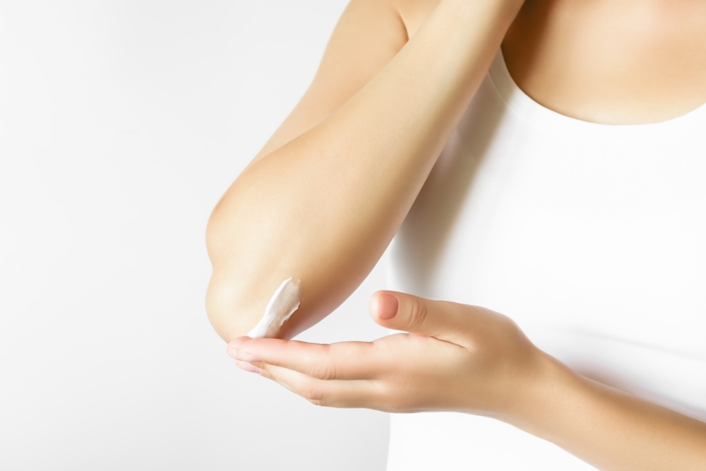 Woman applying lotion to her elbow.