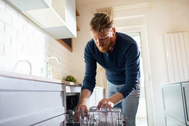 Man loading the dishwasher at home.