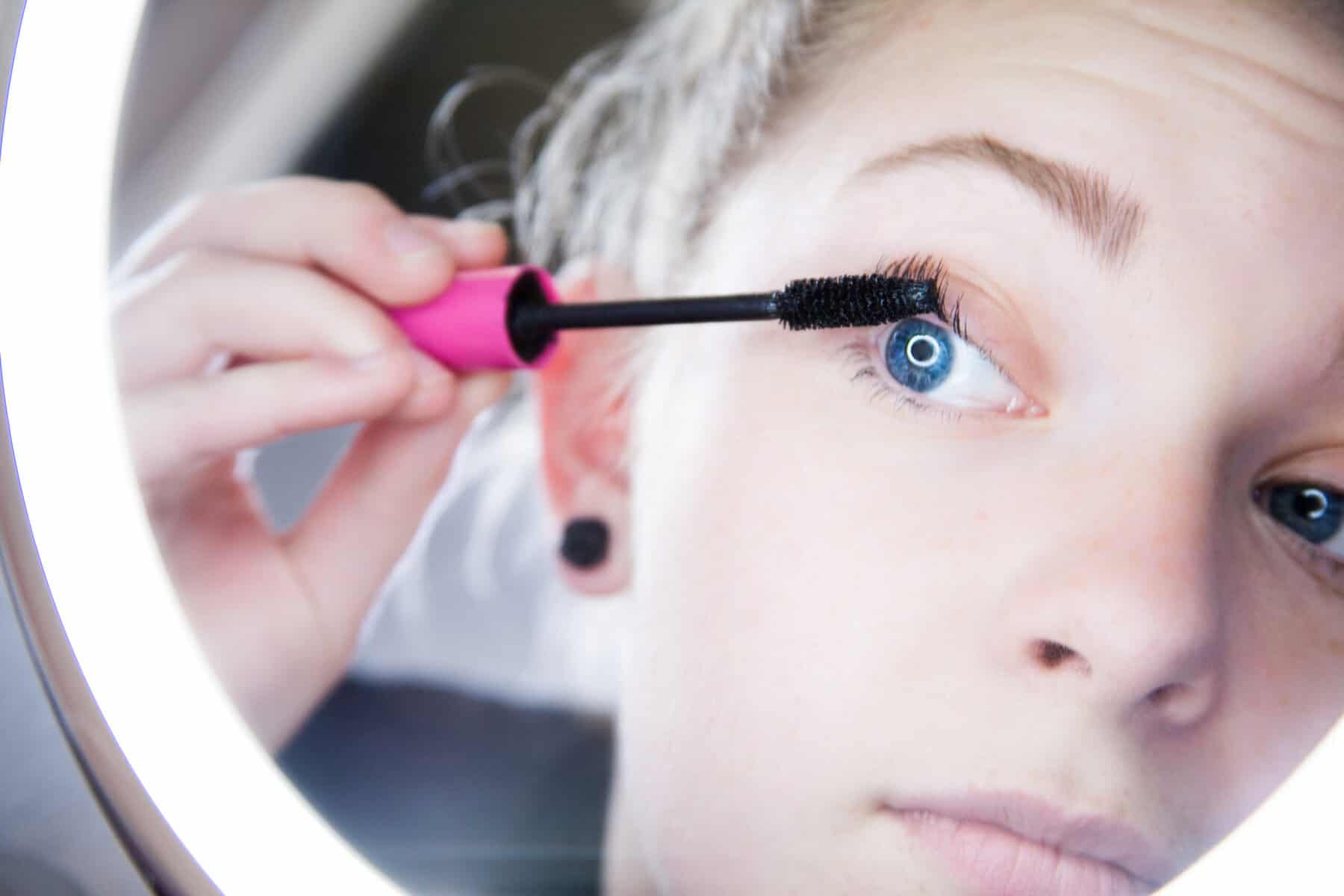 Woman applying mascara in the mirror. 