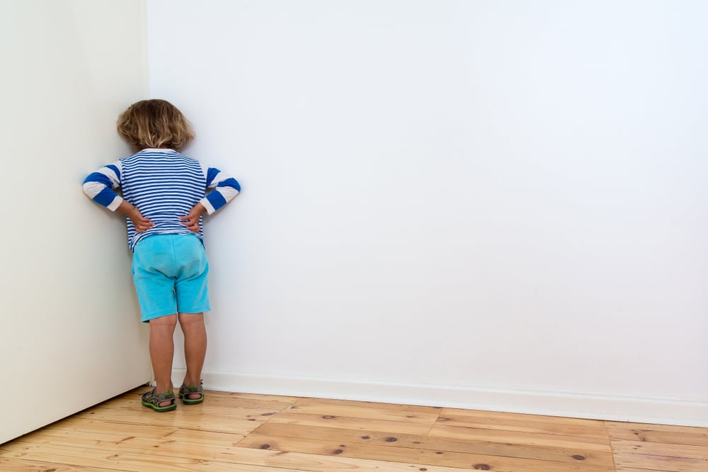 A child punished by his parents and told to stand in the corner, facing the wall