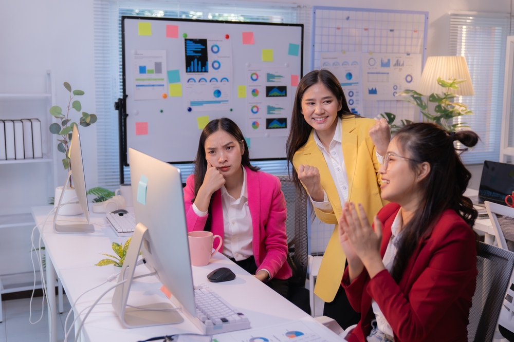 Two happy businesswomen celebrating their success, while their colleague looks on with envy.