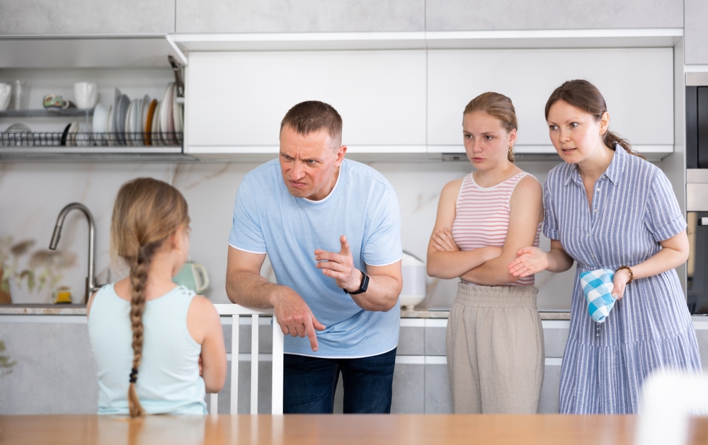 Displeased mother and father reprimanding preteen girl while standing with their teenage daughter
