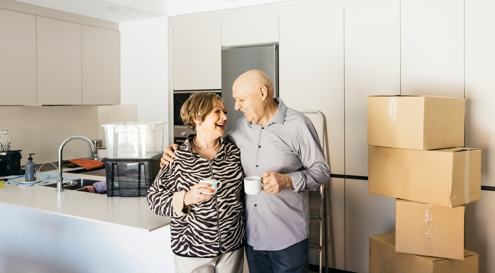 An elderly couple embracing and downsizing and packing items into moving boxes