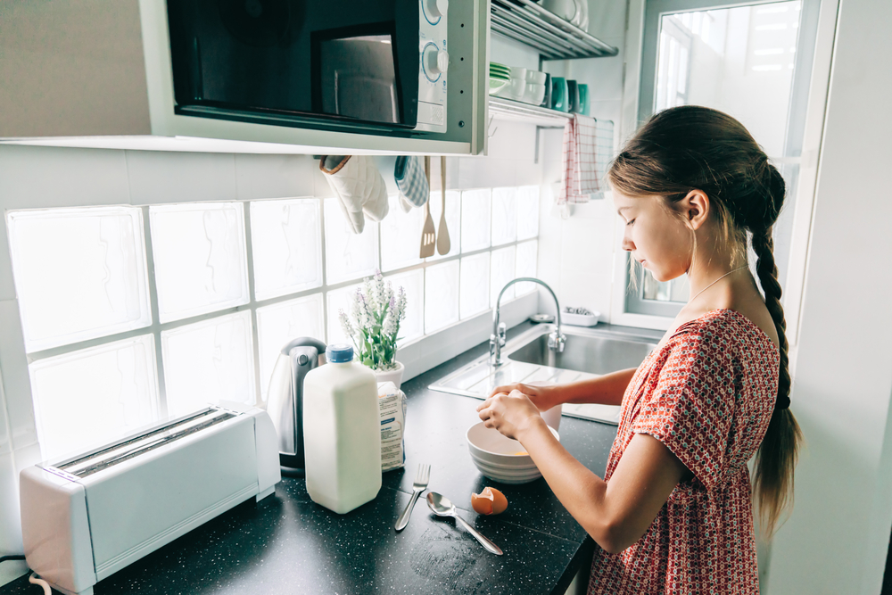 A 10-year old girl alone in the kitchen breaking eggs to make breakfast