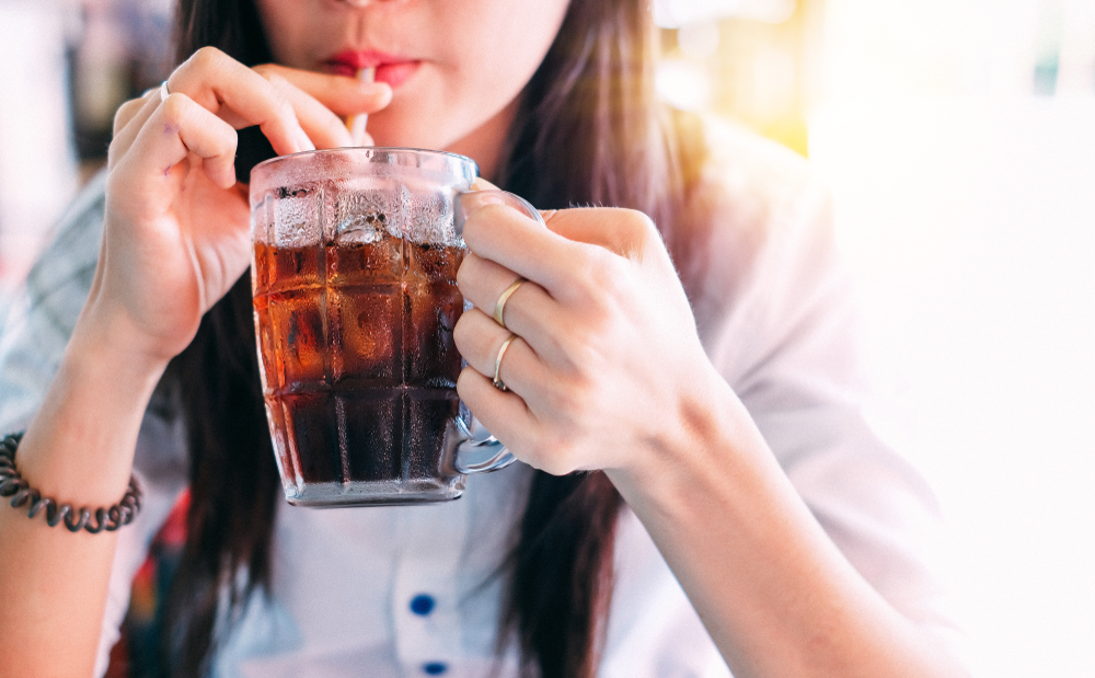 Woman drinking soda, cola, from a straw with ice.