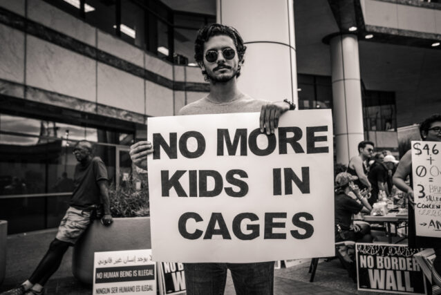 Male protester holding poster saying " No More Kids in cages" in reference to ICE raids