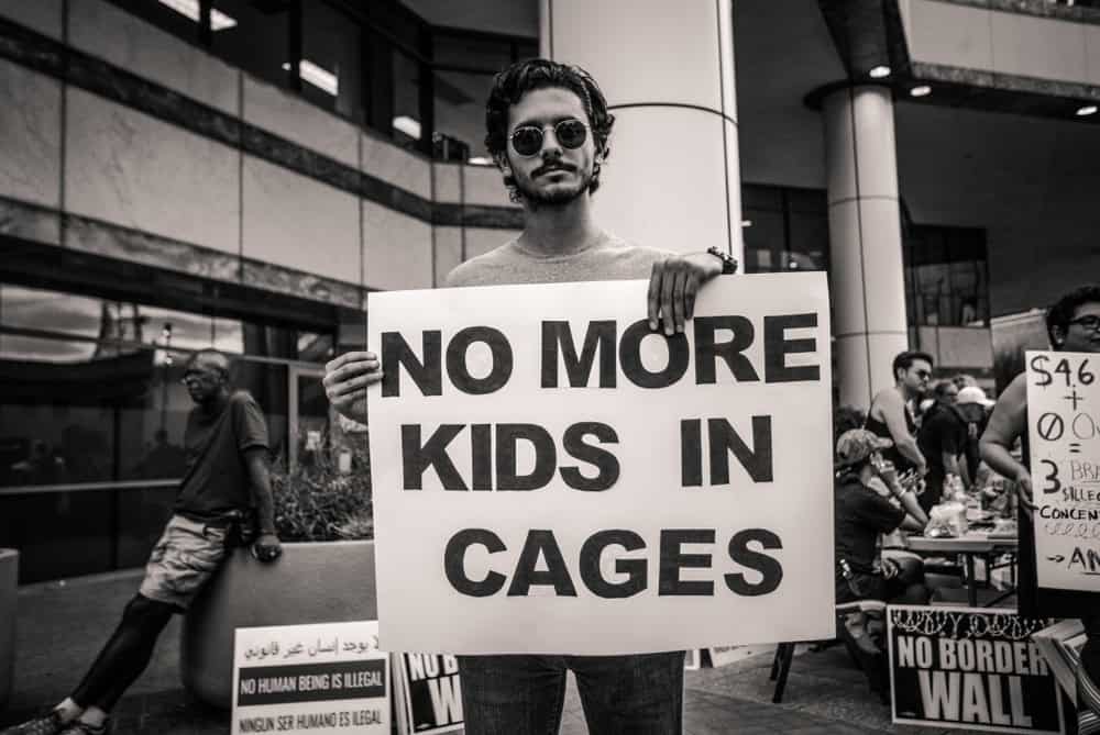 Male protester holding poster saying " No More Kids in cages" in reference to ICE raids