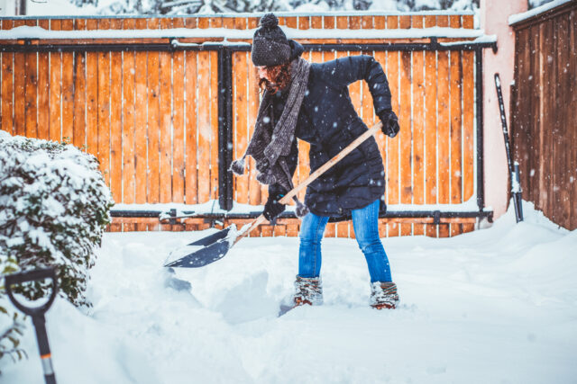 Woman using shovel to clear snow on driveway.