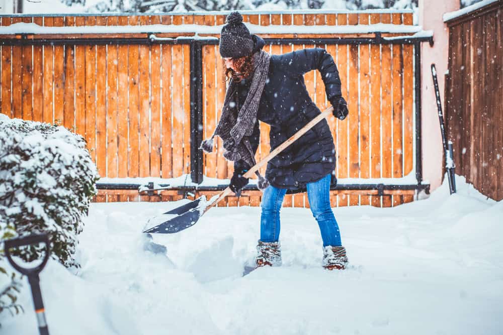 Woman using shovel to clear snow on driveway.