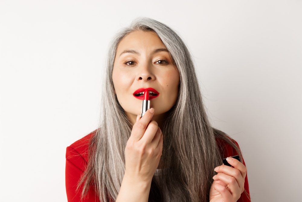Beautiful senior woman with grey hair applying red lipstick.