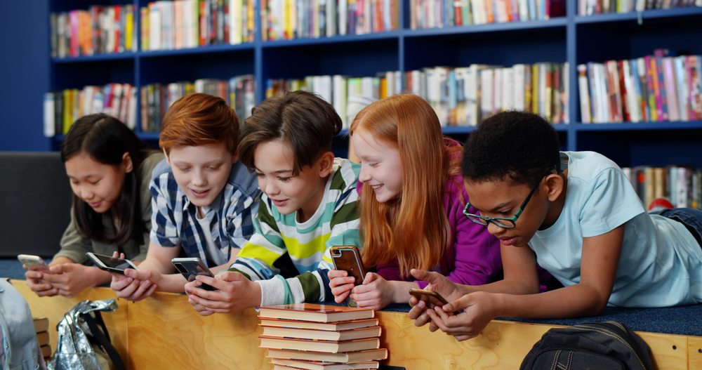 School children, all looking at smartphone laughing and smiling