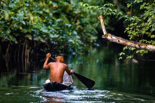 Native Amazon Tribal man using handmade paddle to row handmade boat.