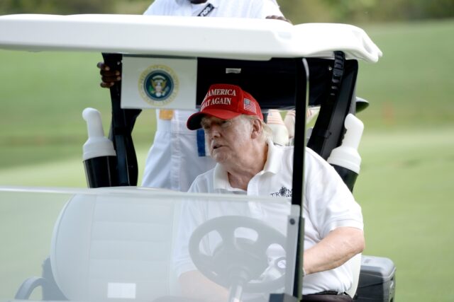 Donald Trump riding in golf cart on golf course.