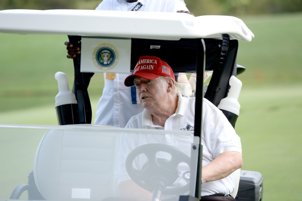 Donald Trump riding in golf cart on golf course.
