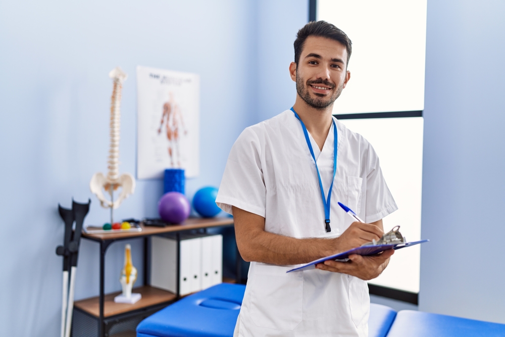 Male Physiotherapist holding clipboard in consultation room.