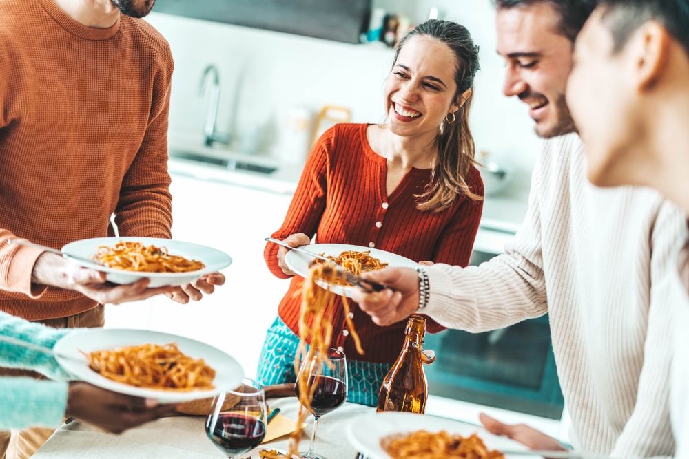 Happy group of friends serving themselves spaghetti at a dinner party.