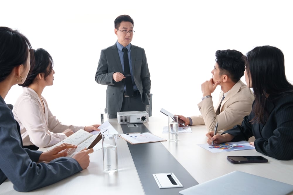 A business team meeting with the obvious leader at the head of the table, standing