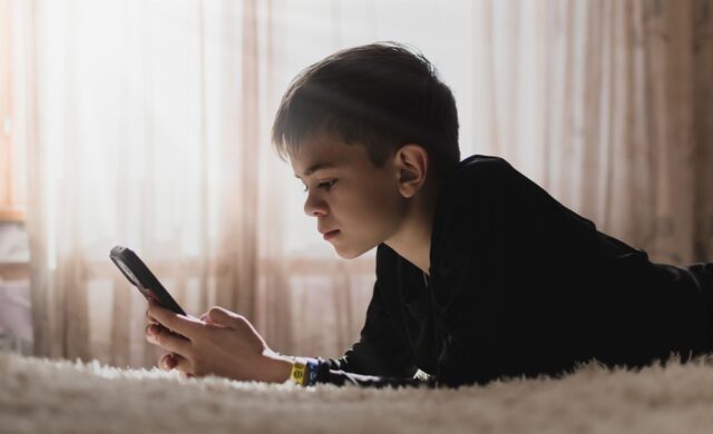 Young boy is lying on the couch and playing with his phone.
