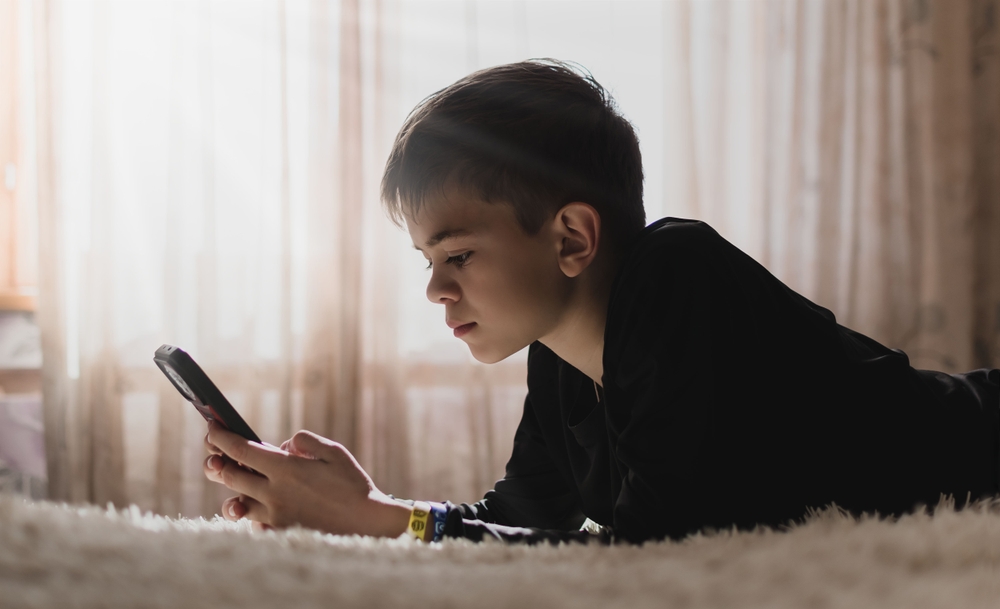 Young boy lying on the couch and looking at his phone.