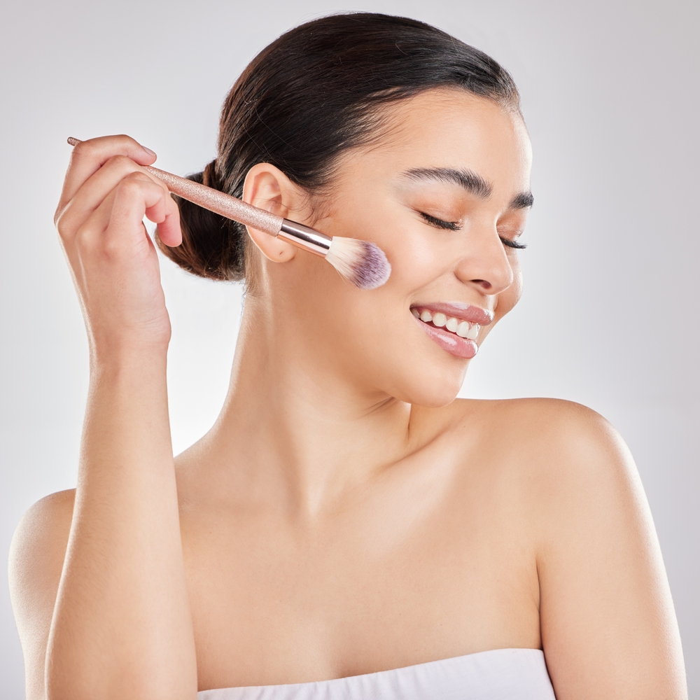 Woman with glowing skin applying blush to her cheeks.