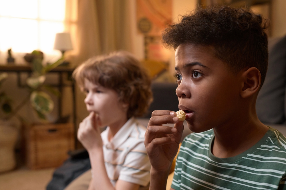 Two children at home in retro living area, watching Tv eating popcorn,