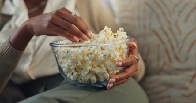 lady's hand in bowl of popcorn, while relaxed on sofa.