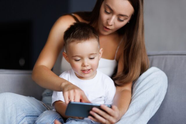 Mother showing young toddler her smartphone.