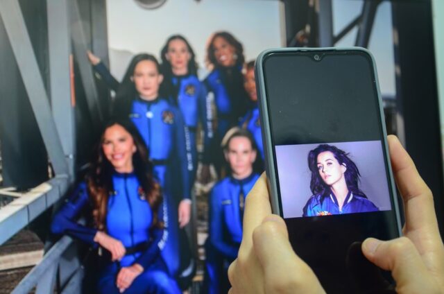Person holding smartphone to watch news about Katy Perry successfully flying into space and returning to Earth aboard the Blue Origin spacecraft. 