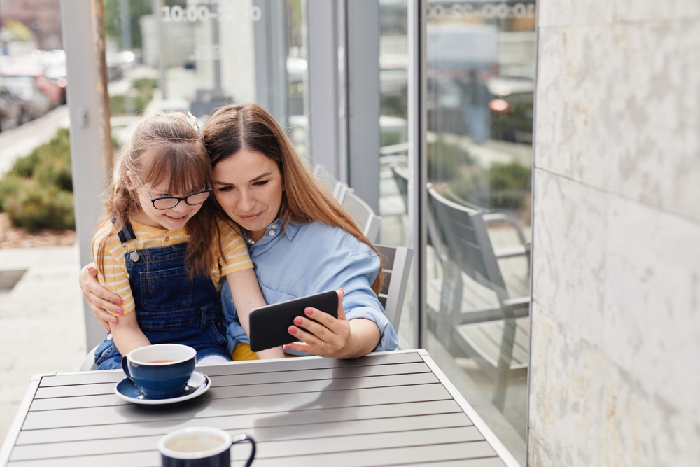 Mother embracing girl with down syndrome while sitting at an outdoor cafe.