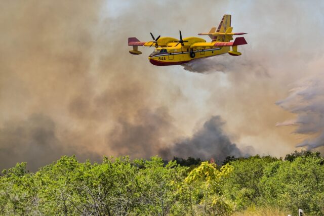 An aerial firefighting plane in action over a forest fire.