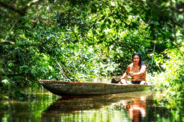 Amazonian Indigenous tribe paddle canoe in river.