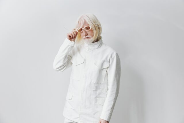 Male fashion model with white hair wears all white suit and white sunglasses.