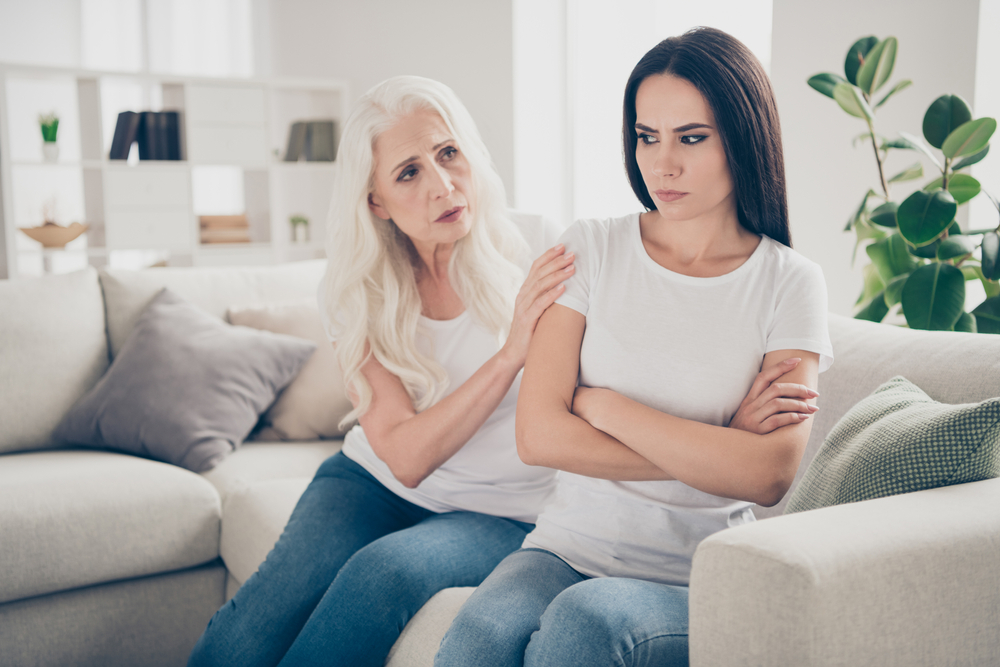 A young girl irritated by her mother and turns her back to her, the mother touches her shoulder and tries to pacify her